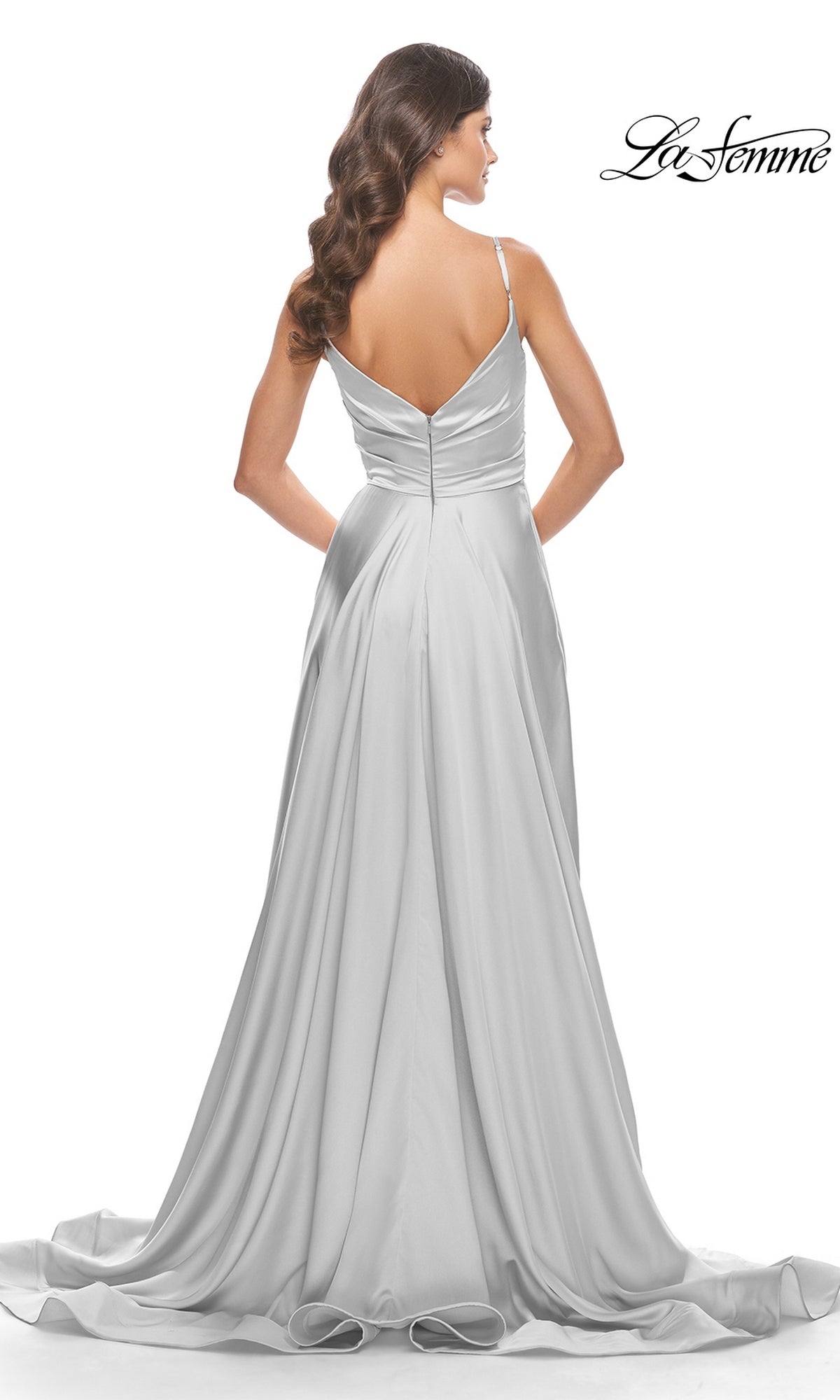 A woman wears the La Femme V-Neck Long A-Line Prom Dress 31505, a floor-length silver satin gown with thin straps, V-shaped back, and flowing train, standing against a white background.